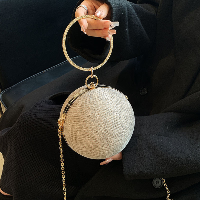 A person holds a sparkling light gold spherical clutch with a large gold ring handle.