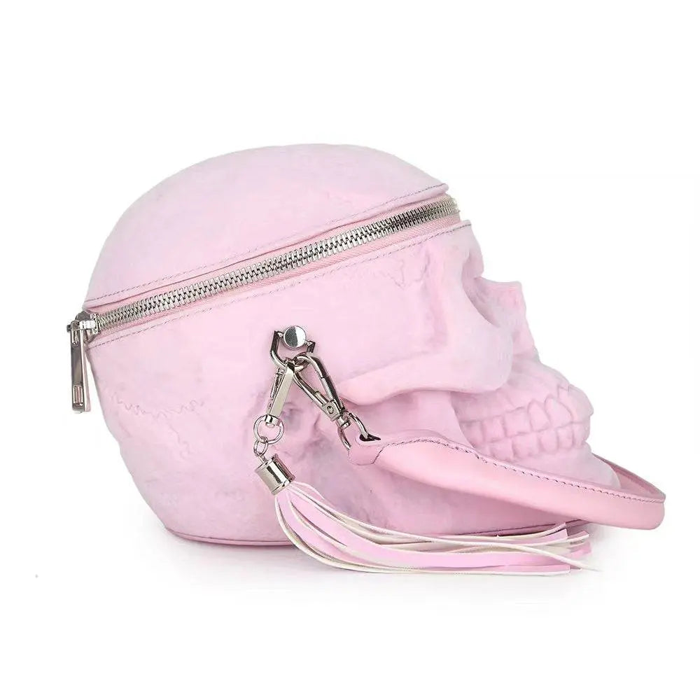 Pink suede skull-shaped crossbody bag with a silver zipper and tassel.