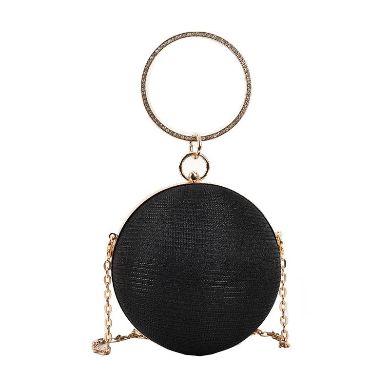 Black circular evening clutch with a textured gold ring handle and chain strap.