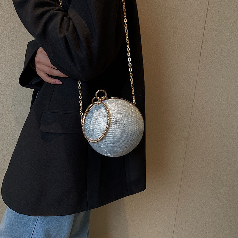 Sparkling silver spherical clutch with gold metal chain and ring.
