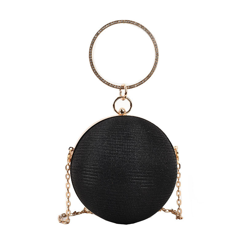 Black circular evening clutch with a textured finish, gold metal ring handle, and chain.