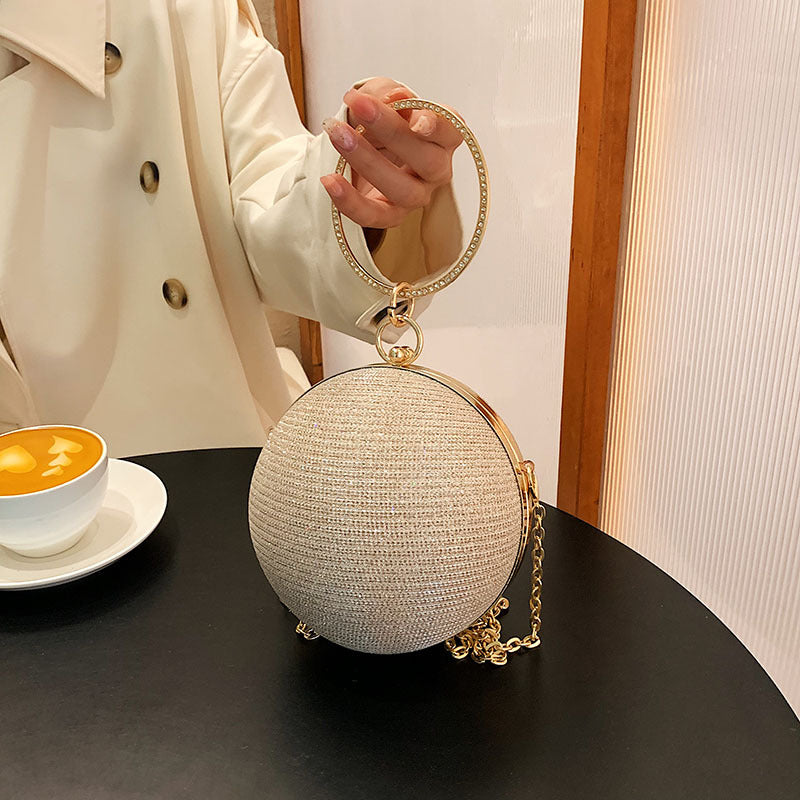 Light gold circular clutch with a sparkling ring handle and chain strap.