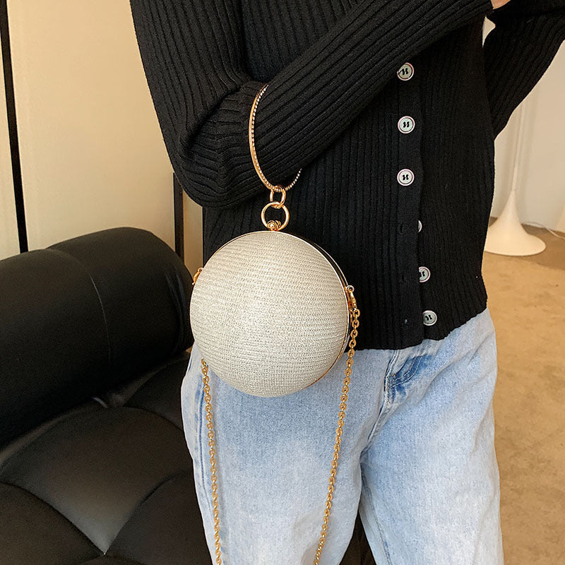 Textured light beige spherical clutch with gold ring handle and chain.